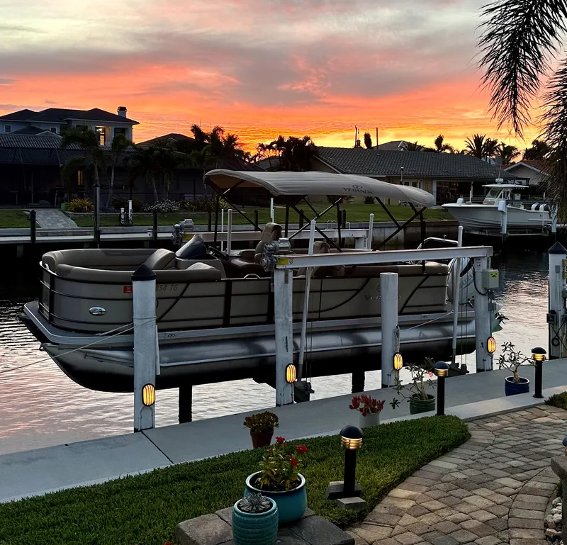 Slide: The Image of 2022 Veranda Relax VR22RC pontoon boat docked at sunset, surrounded by waterfront homes. - 1