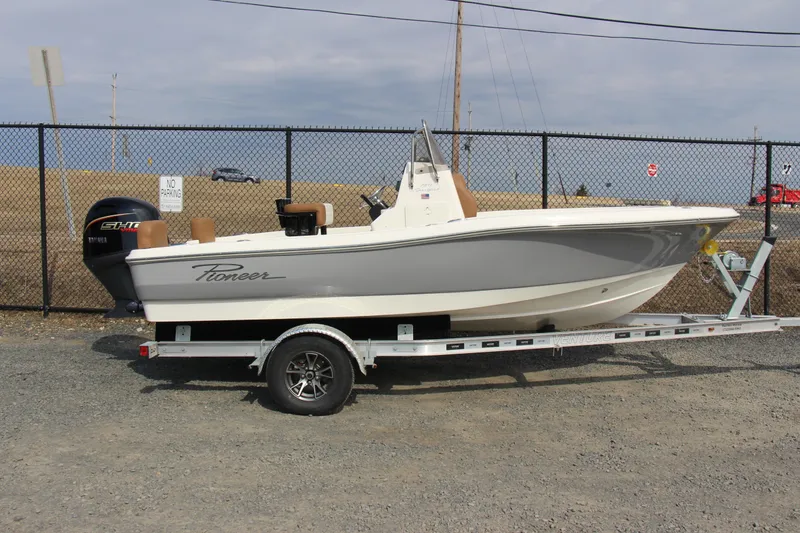 Slide: The Image of 2025 Pioneer 180 Sportfish boat on trailer, parked near a chain-link fence. - 0