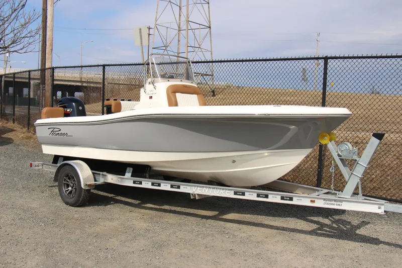 Slide: The Image of 2025 Pioneer 180 Sportfish boat on trailer, parked near a chain-link fence. - 4