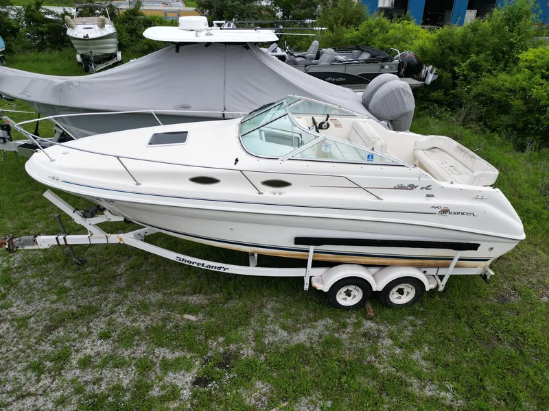 Slide: The Image of 1998 Sea Ray 240 Sundancer boat on trailer, parked on grass, surrounded by other boats. - 0