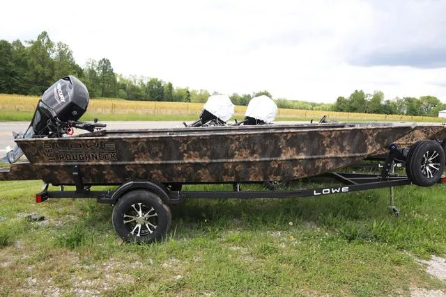 Slide: The Image of 2024 Lowe Roughneck 1660 Tiller boat on trailer, camo design, parked outdoors. - 3