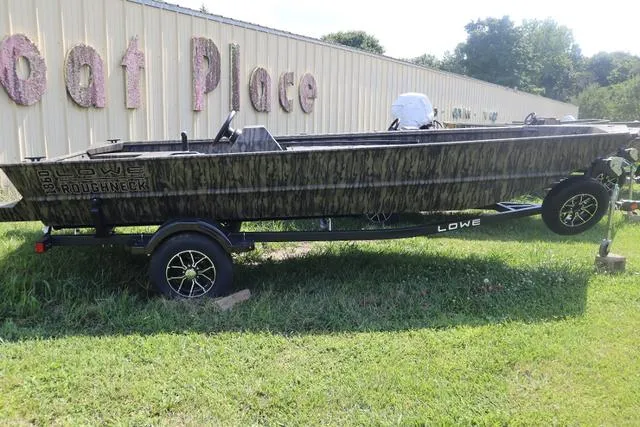 Slide: The Image of 2025 Lowe Roughneck 1860 Add-On Console boat on trailer, parked outdoors near a building. - 3