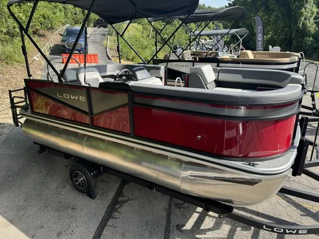Slide: The Image of 2025 Lowe LS 170 pontoon boat with red exterior, parked on a trailer. - 1