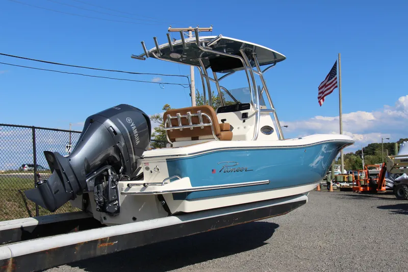 Slide: The Image of 2025 Pioneer 222 Sportfish boat on trailer, blue hull, outboard motor, American flag in background. - 2