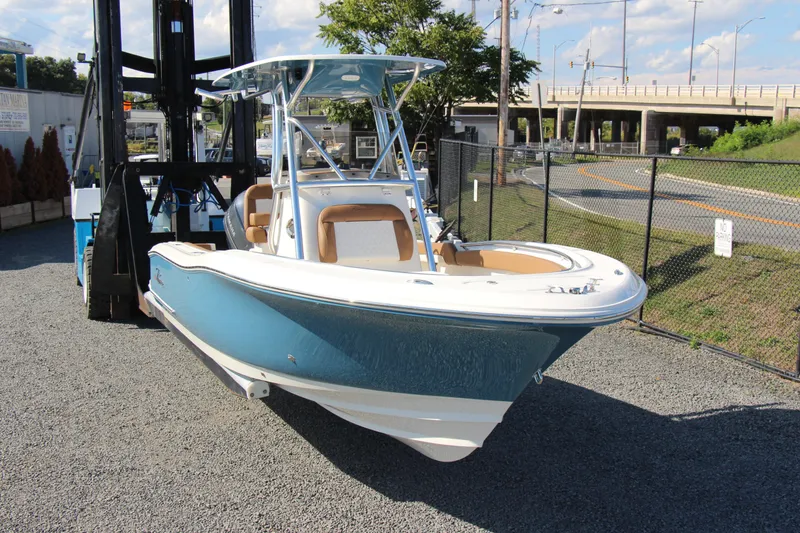 Slide: The Image of 2025 Pioneer 222 Sportfish boat with blue hull, parked on gravel near a fence. - 4