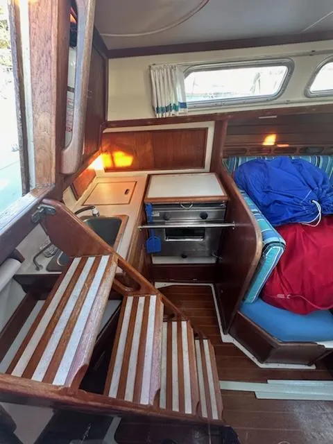 Slide: The Image of Interior of 1985 Ericson 30 Plus sailboat, featuring wooden stairs, compact kitchen, and cozy seating area. - 13
