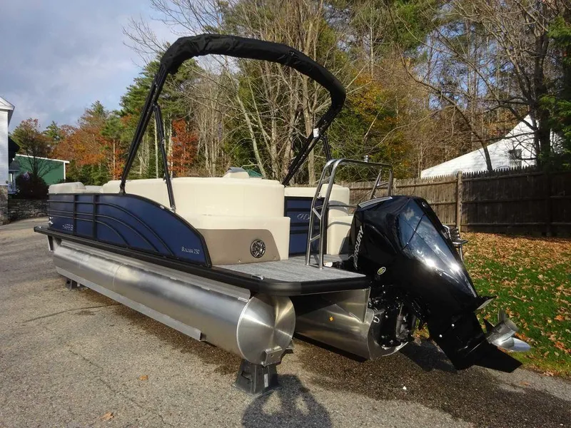 Slide: The Image of 2024 Harris Sunliner 230 pontoon boat with outboard motor, parked on a driveway. - 4