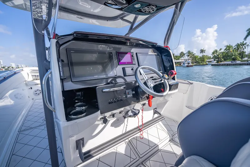 Slide: The Image of 2018 Nor-Tech 390 boat cockpit with modern navigation system and steering wheel, docked by a scenic waterway. - 36