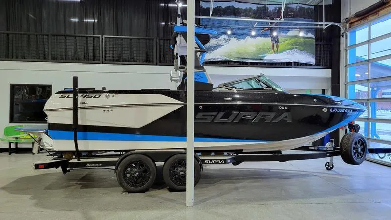 Slide: The Image of 2018 Supra SL 450 boat in showroom, black and blue design, on trailer. - 3
