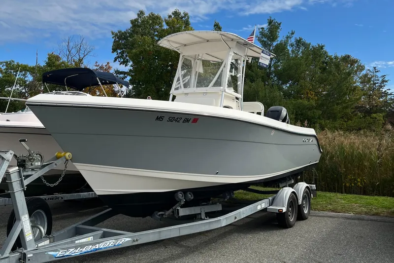 Slide: The Image of 2012 Cobia 237CC boat on trailer, parked outdoors with trees in the background. - 0