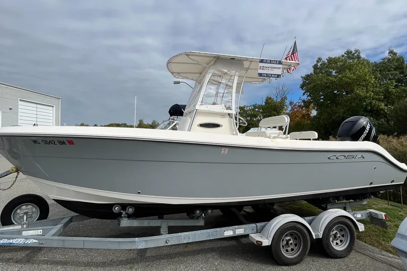 Slide: The Image of 2012 Cobia 237CC boat on trailer, parked outdoors, with American flag in background. - 1