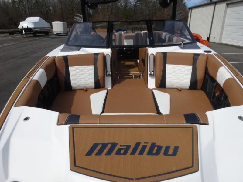 Slide: The Image of 2025 Malibu 24 MXZ boat interior with tan and white seating, parked outdoors. - 21