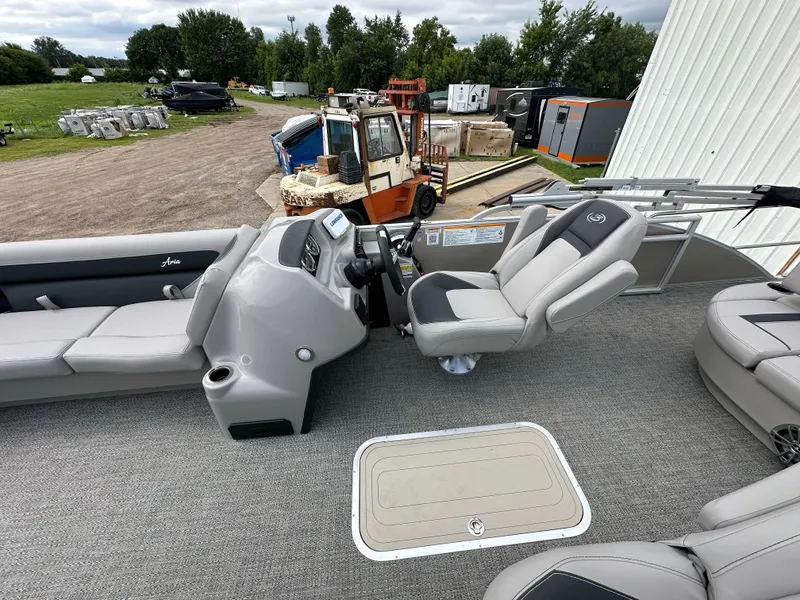 Slide: The Image of 2025 Barletta Aria 24UC pontoon boat interior with helm and seating, parked outdoors. - 15