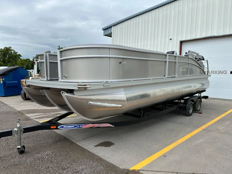 Slide: The Image of 2025 Barletta Aria 24UC pontoon boat on trailer, parked outside a building. - 28