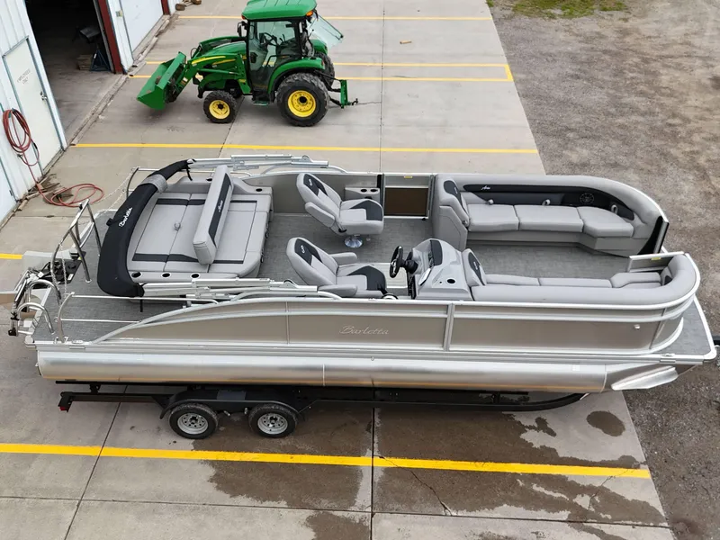 Slide: The Image of 2025 Barletta Aria 24UC pontoon boat on trailer, parked near green tractor. - 3