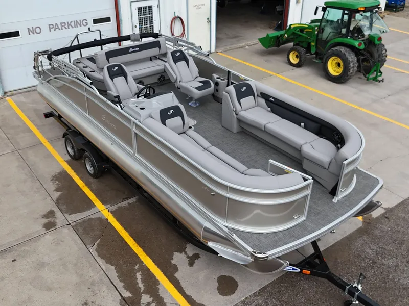 Slide: The Image of 2025 Barletta Aria 24UC pontoon boat on trailer, parked near a green tractor. - 6