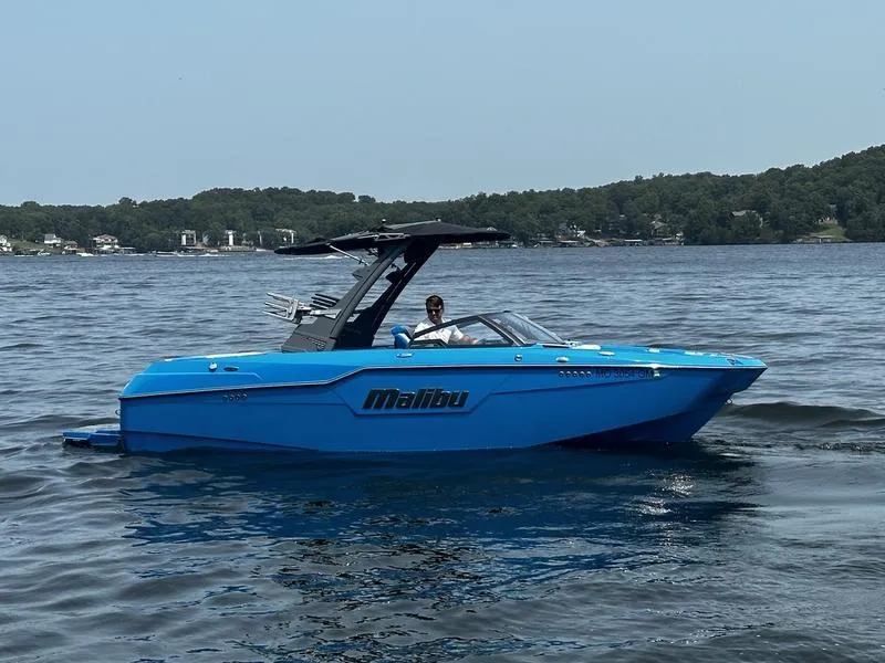 The Image of Blue 2021 Malibu M220 boat cruising on a lake with forested shoreline. - 0