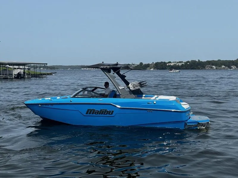 Slide: The Image of 2021 Malibu M220 boat in blue on a lake, with a person onboard. - 1