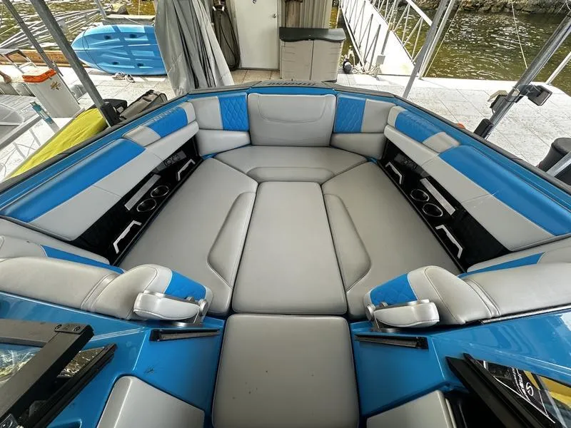 Slide: The Image of 2021 Malibu M220 boat interior with blue and gray seating, docked by the water. - 10