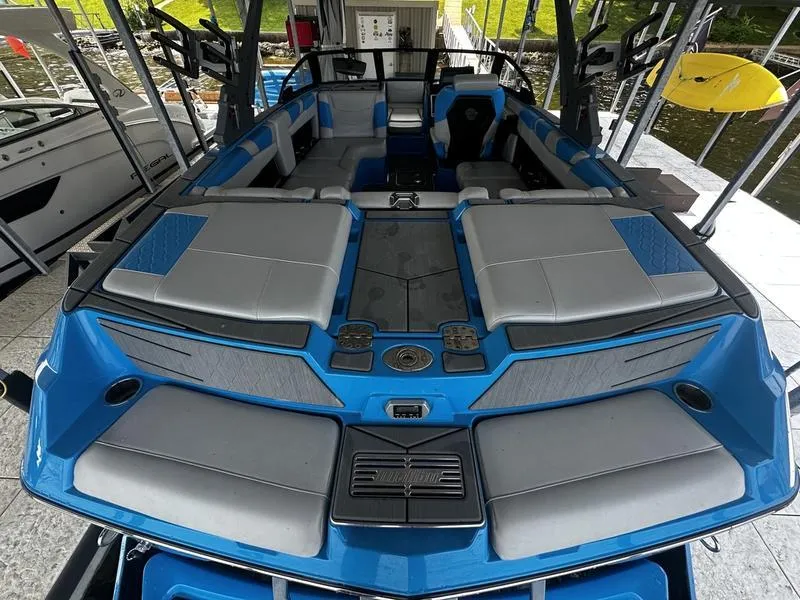 Slide: The Image of 2021 Malibu M220 boat interior with blue and gray seating, docked by the water. - 20