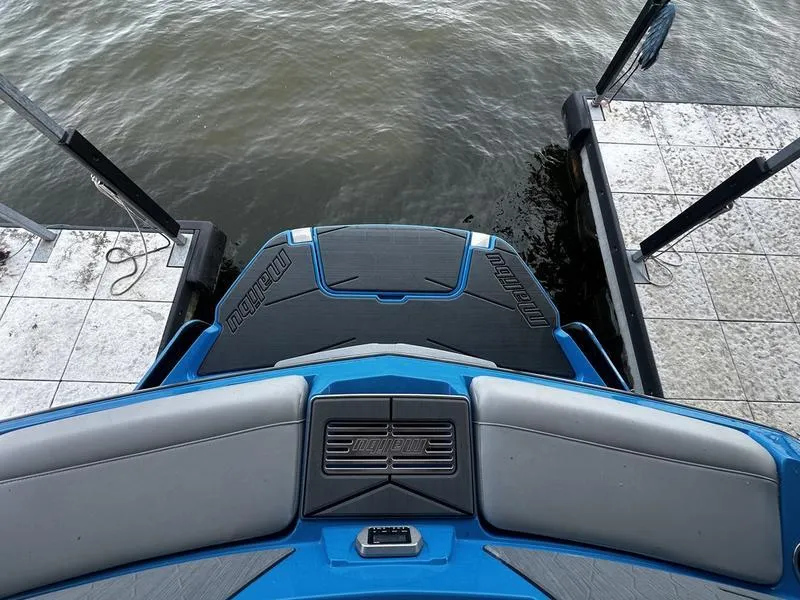 Slide: The Image of 2021 Malibu M220 boat stern view at dock, featuring blue and gray seating. - 22