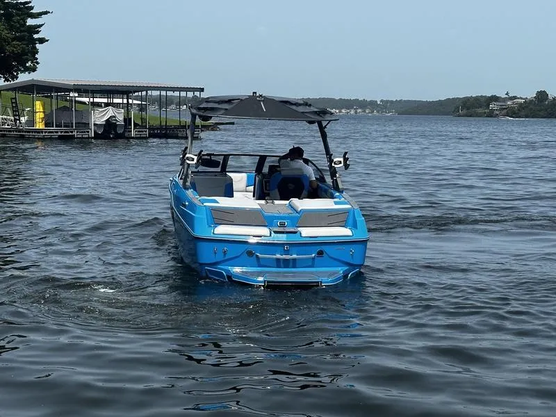 Slide: The Image of 2021 Malibu M220 boat on a lake, blue exterior, near a dock. - 4