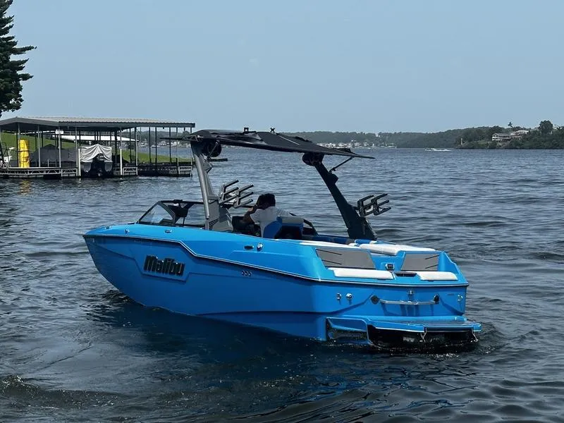 Slide: The Image of 2021 Malibu M220 boat in blue on a lake, near a dock. - 6