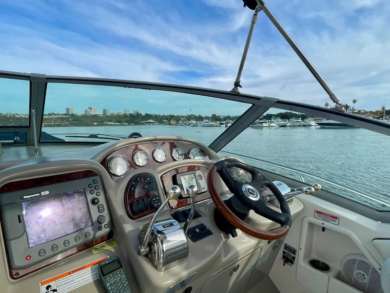 Slide: The Image of 2006 Sea Ray 320 Sundancer helm with navigation equipment, steering wheel, and waterfront view. - 22