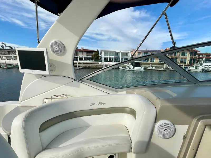 Slide: The Image of 2006 Sea Ray 320 Sundancer boat interior with waterfront view, featuring seating and a mounted screen. - 28