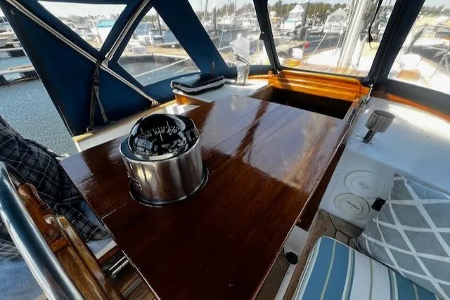 Slide: The Image of 1978 Custom Fantasia C/C Double Ended Cutter cockpit with compass, wooden table, and marina view. - 24