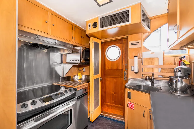 Slide: The Image of 1965 Burger Motoryacht kitchen with wooden cabinetry, stainless steel appliances, and porthole door. - 24