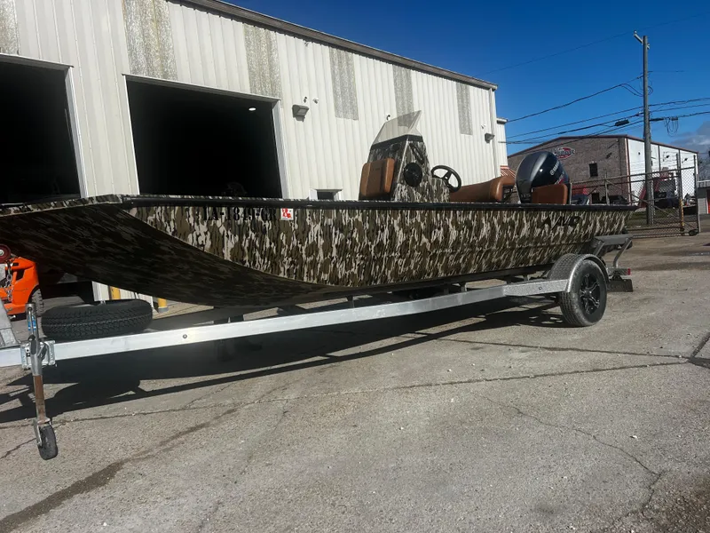 Slide: The Image of 2023 Avid 20 Rogue boat with camouflage design on a trailer outside a warehouse. - 3