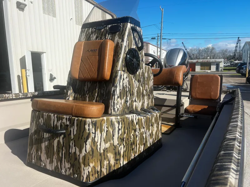 Slide: The Image of 2023 Avid 20 Rogue boat with camouflage design and brown seating, parked outdoors. - 5
