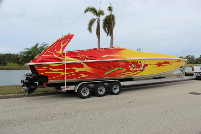 Slide: The Image of 2001 Sonic 42 SS speedboat with vibrant flame design on trailer, parked near palm trees. - 14