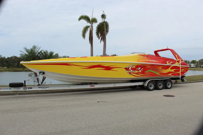 Slide: The Image of 2001 Sonic 42 SS speedboat with vibrant flame design on a trailer by a waterfront. - 59