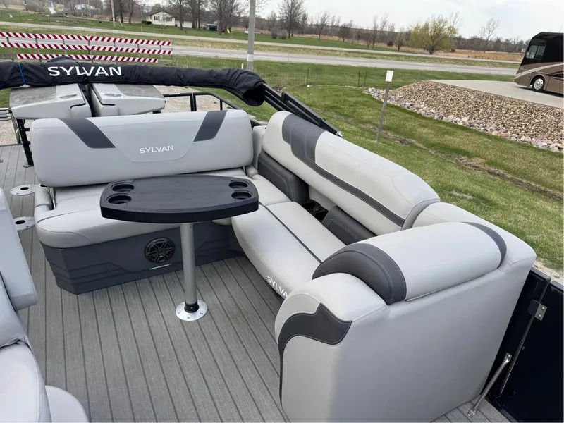 Slide: The Image of 2023 Sylvan L5 DLZ Bar pontoon boat with gray seating and table, parked on grass. - 10