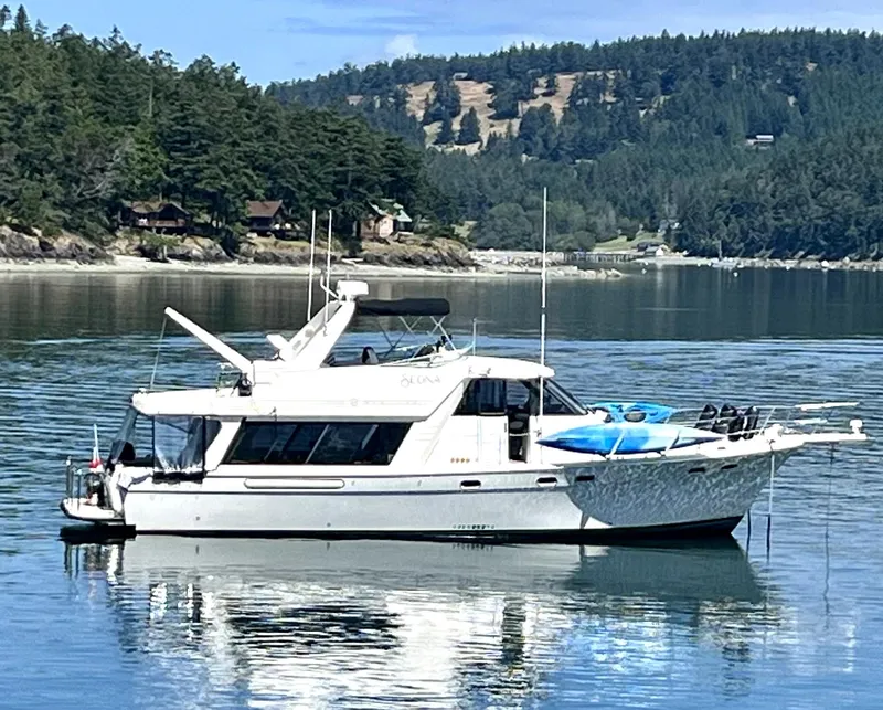 Slide: The Image of 1996 Bayliner 4788 Pilothouse yacht on serene water with forested shoreline background. - 3