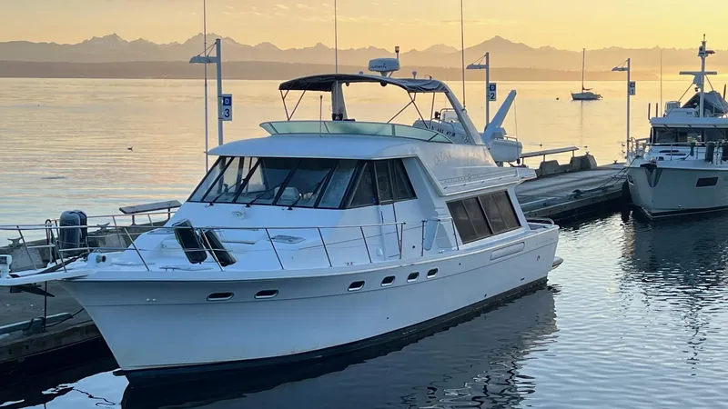 Slide: The Image of 1996 Bayliner 4788 Pilothouse yacht docked at sunset with scenic mountain backdrop. - 4
