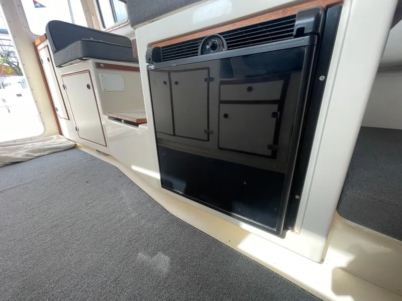 Slide: The Image of 2009 C-Dory TOMCAT 255 interior with compact black refrigerator and seating area. - 33