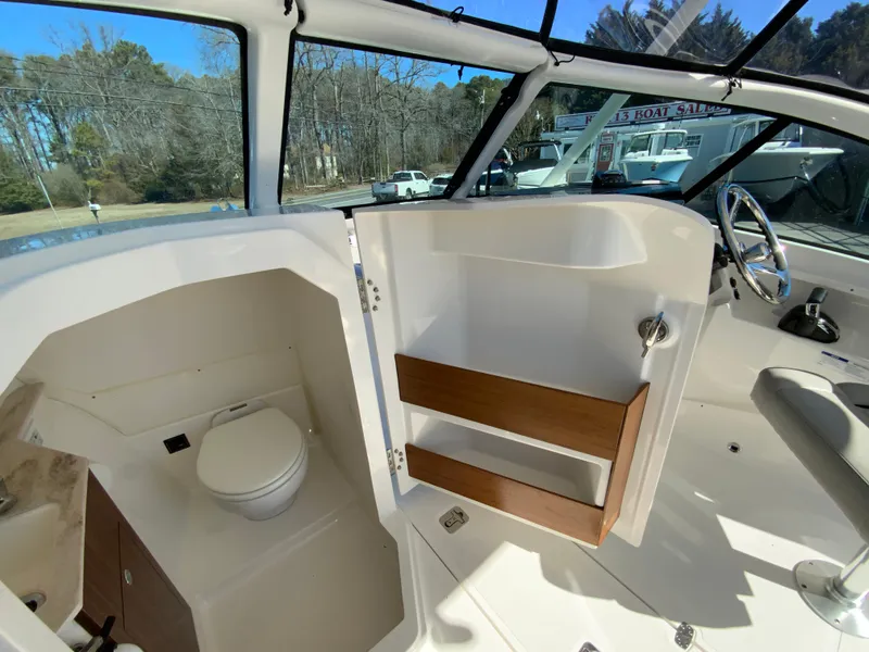 Slide: The Image of 2024 Pursuit DC 246 Dual Console boat interior with open door revealing compact toilet. - 33