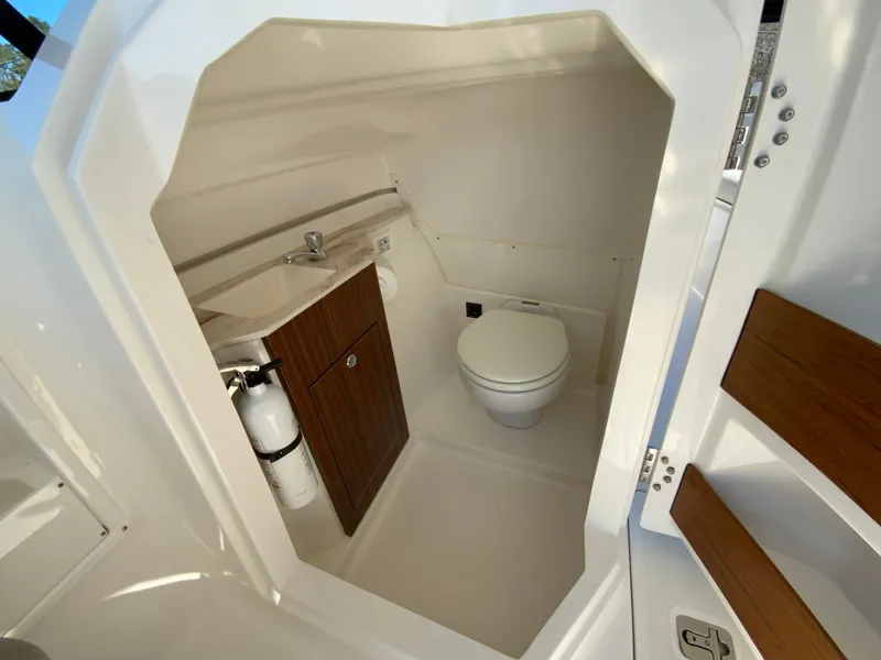 Slide: The Image of 2024 Pursuit DC 246 Dual Console boat interior with compact bathroom and wooden cabinetry. - 34