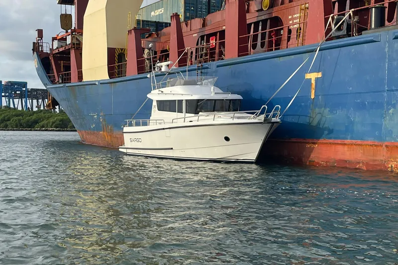 Slide: The Image of Sargo 36 Flybridge 2015 yacht moored beside a large cargo ship in calm waters. - 2