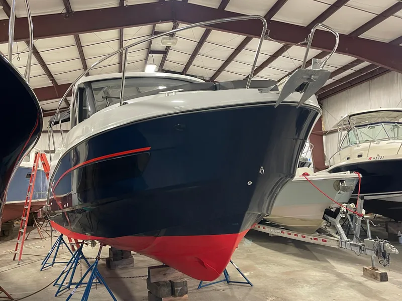 Slide: The Image of 2022 Beneteau Antares 9 boat in storage, blue hull with red accents. - 2