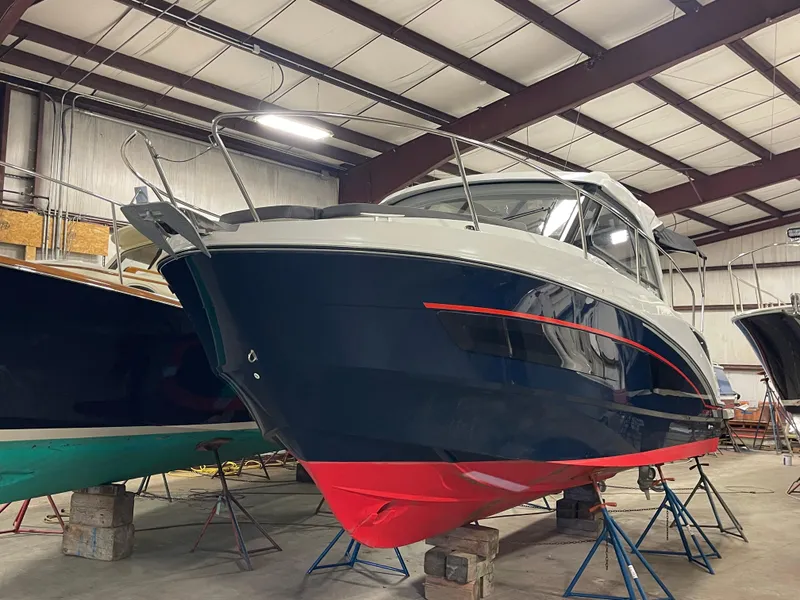 Slide: The Image of 2022 Beneteau Antares 9 boat in storage, blue and red hull, indoor facility. - 4