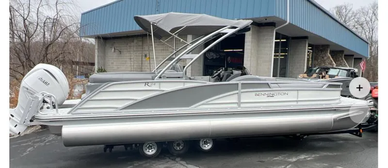 The Image of 2025 Bennington R 24 RTFBA pontoon boat with Yamaha outboard motor, parked outside a building. - 1