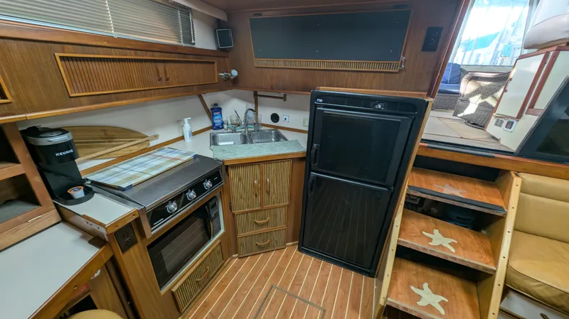 Slide: The Image of 1987 Sea Ray 390 Express Cruiser interior with kitchen, stove, fridge, and wooden cabinetry. - 15