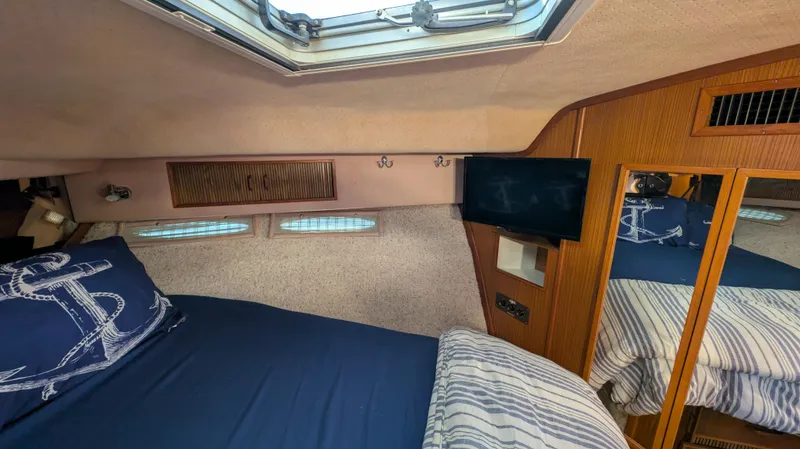 Slide: The Image of 1987 Sea Ray 390 Express Cruiser cabin with bed, skylight, TV, and wooden accents. - 23