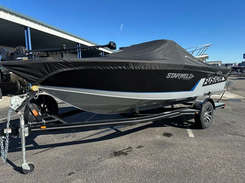 Slide: The Image of 2025 Starweld Fusion 18 DC boat on trailer, covered, parked outdoors. - 2