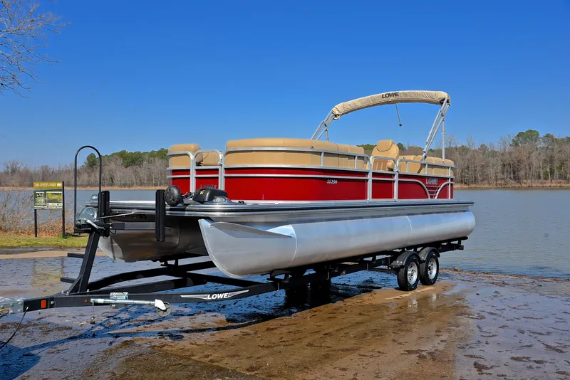 Slide: The Image of 2021 Lowe SS250 pontoon boat on trailer by a lake, under clear blue sky. - 10