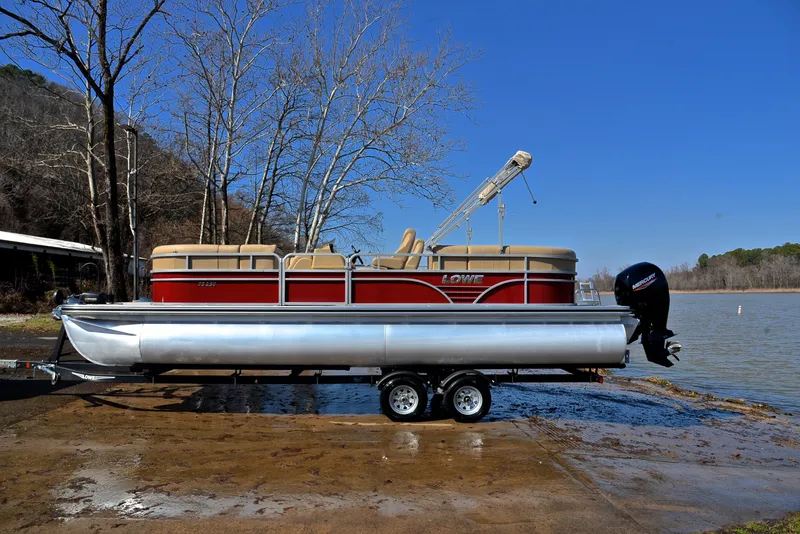 Slide: The Image of 2021 Lowe SS250 pontoon boat on trailer by a lake, under clear blue sky. - 11